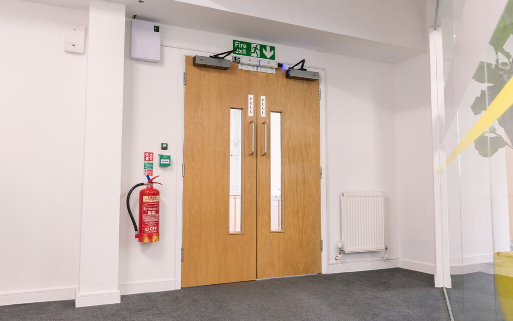 A close-up shot of a compliant communal fire door in an apartment hallway, showing clear safety signage and a properly installed self-closing device